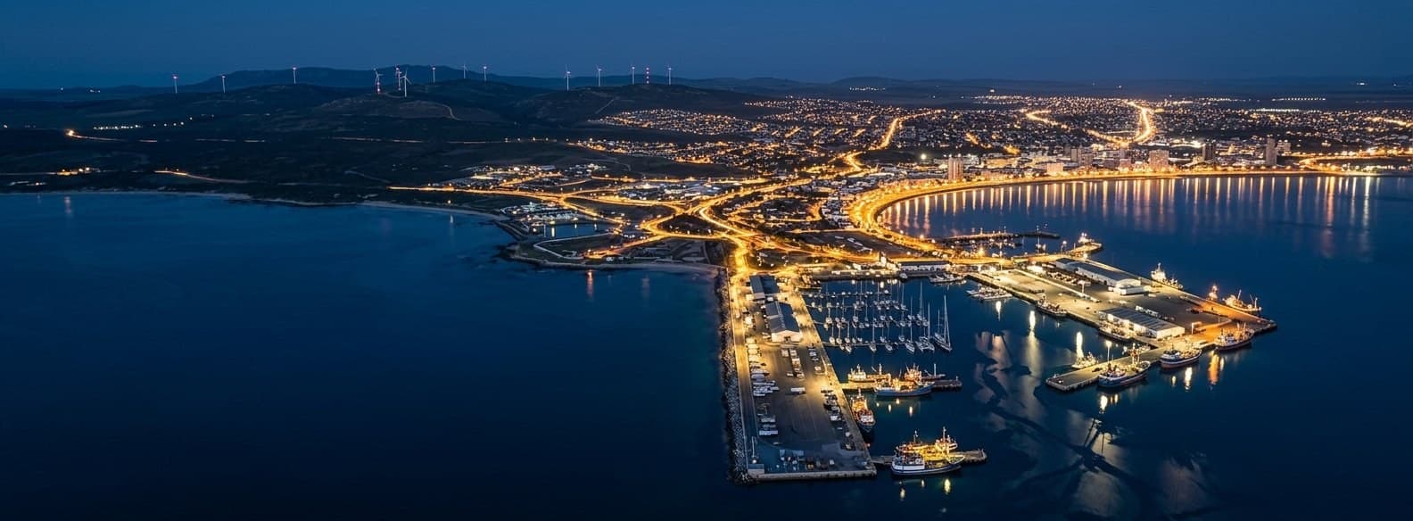 Harbor at night with illuminated wind turbines along the waterfront